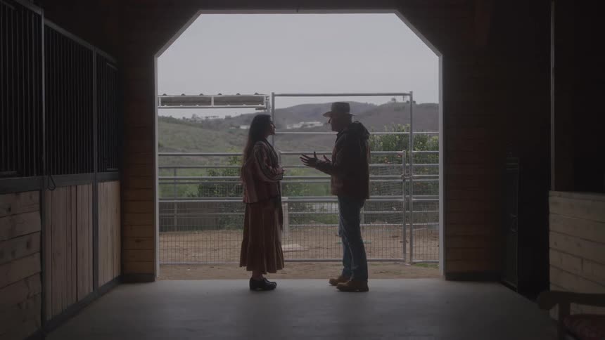 Two people talking in front of a fence with hills in the background