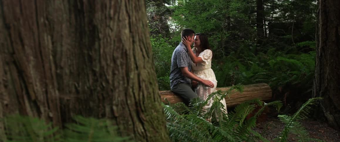 A man and woman kiss on a tree stump