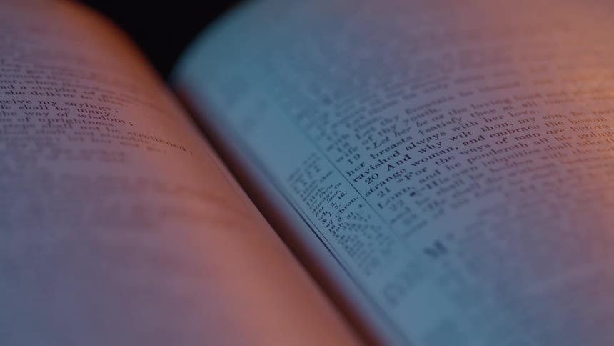 Open pages of an old book illuminated by blue and orange light
