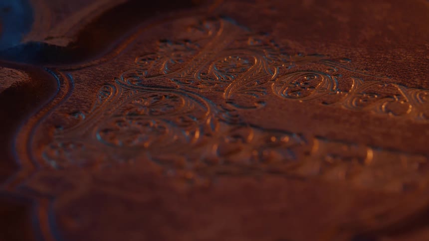 Ornate embossed details on the cover of an old book under warm and bluish light