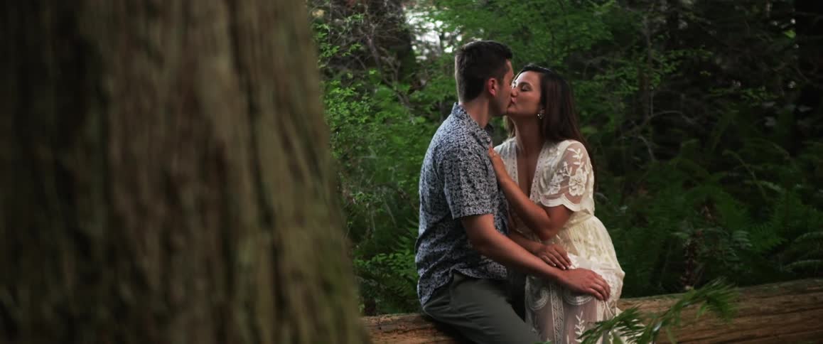 A man and woman are sitting on a log kissing and caressing each other