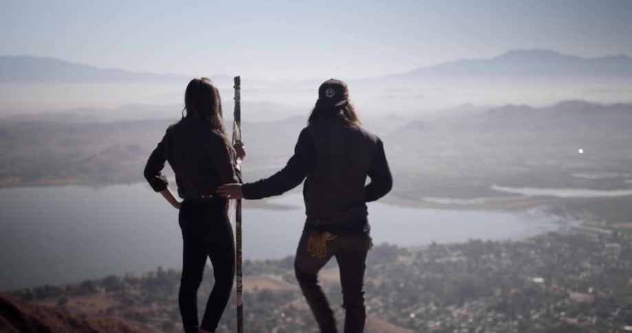 Man and woman standing on top of a mountain overlooking a lake