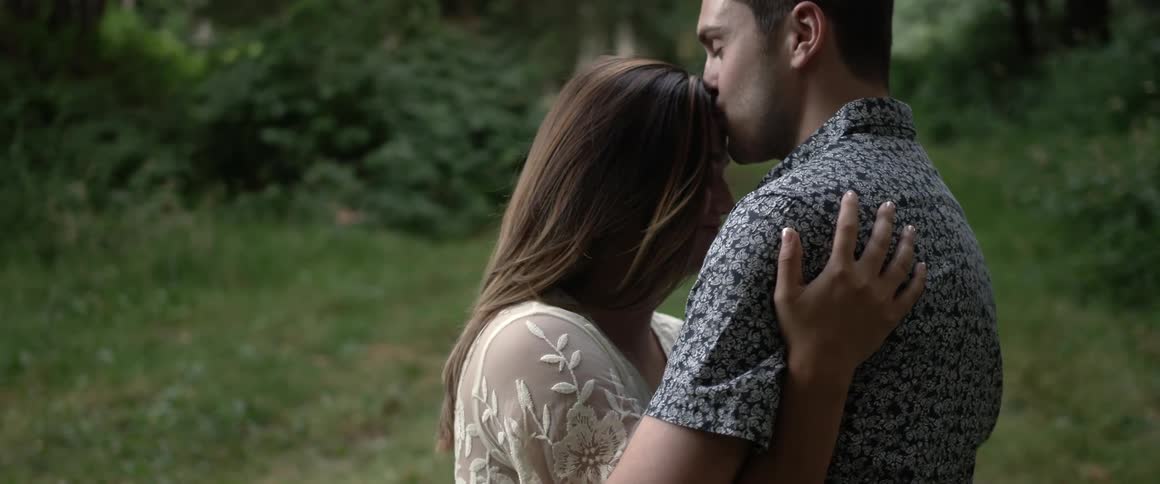 A man and woman embrace in a forested area