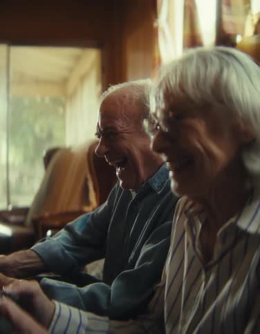 An elderly couple laughs together while playing a video game indoors