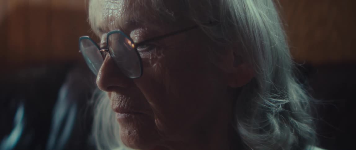 An elderly woman on a couch with a sad expression indoors