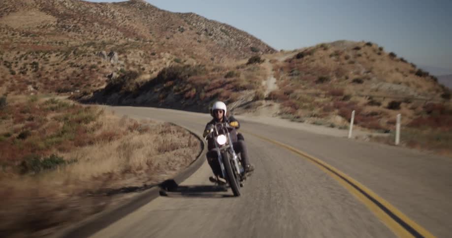 A man and woman ride a motorcycle through a hilly area