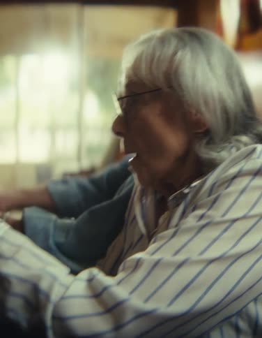 Close up of an elderly man and woman playing video games with a controller while sitting together in a living room during daytime
