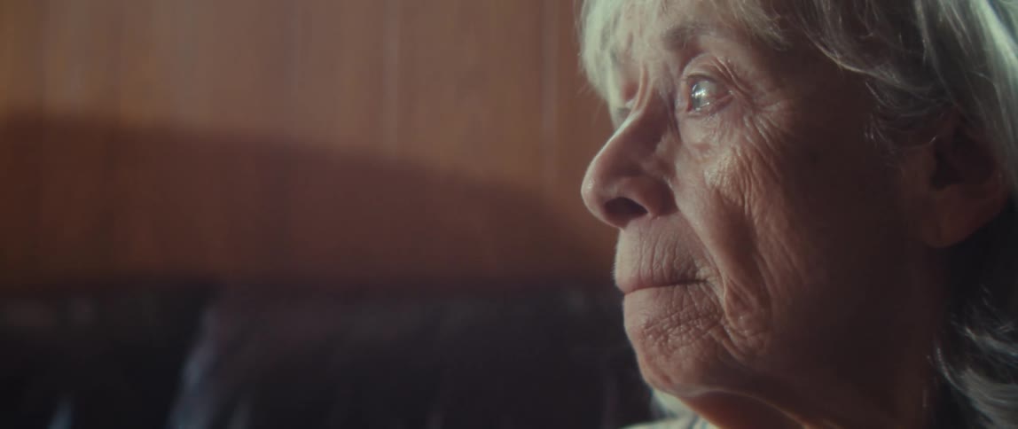 An elderly woman sits sad and emotional on a couch indoors