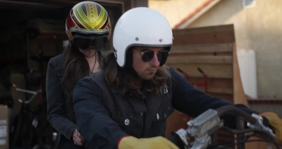 Woman climbs onto motorcycle behind a man and they ride off