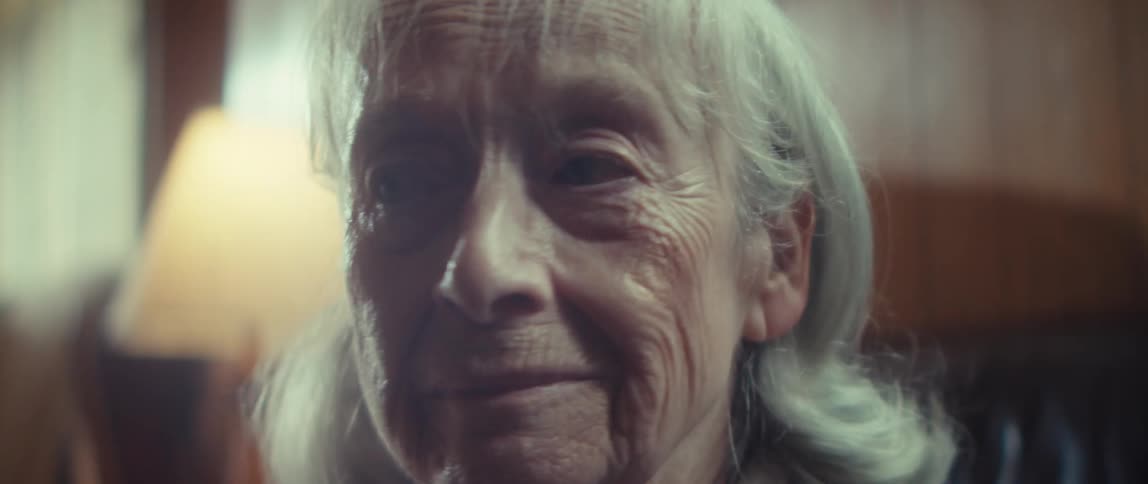 Elderly woman sitting in her living room frowns to the side before facing forward