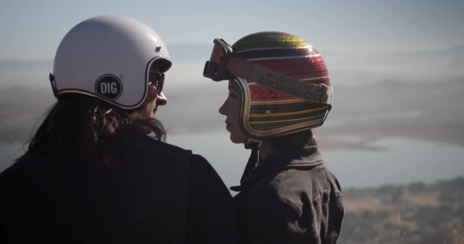 A man and woman wearing motorcycle helmets look at the view