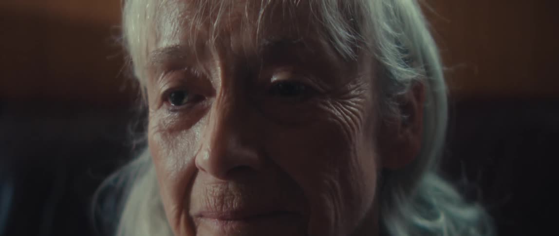 Close up of an elderly woman sitting contemplatively on a couch in a living room during daytime