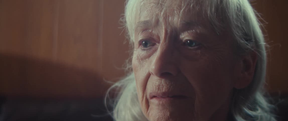 An elderly person seated on a couch with a sad expression in living room