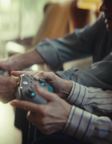 Close up of an elderly man and woman playing a video game with controllers while sitting in a living room during daytime