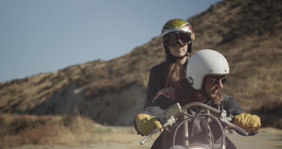 A woman climbs onto the back of a motorcycle