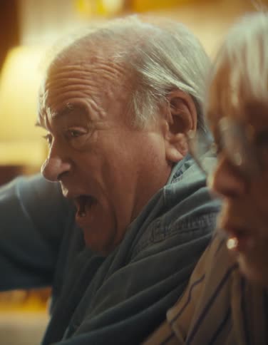 Close up of an elderly man and woman playing video games with controllers while sitting in a living room during daytime