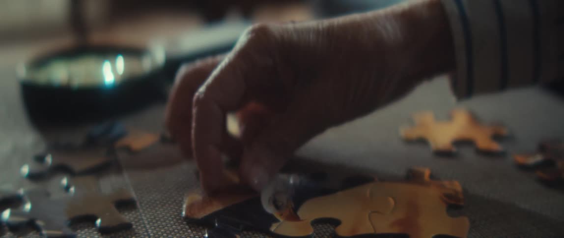 A closeup of a hand placing a puzzle piece on a table indoors