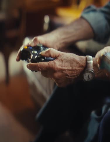 Close up of an elderly man and woman playing video games with a controller while sitting in a living room during daytime