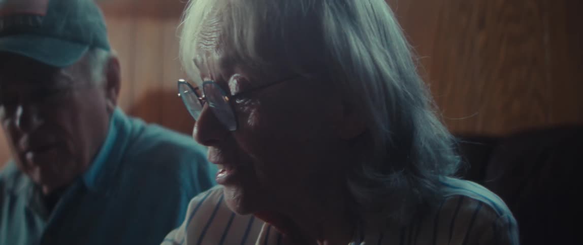 An elderly couple talks quietly on a couch in a living room