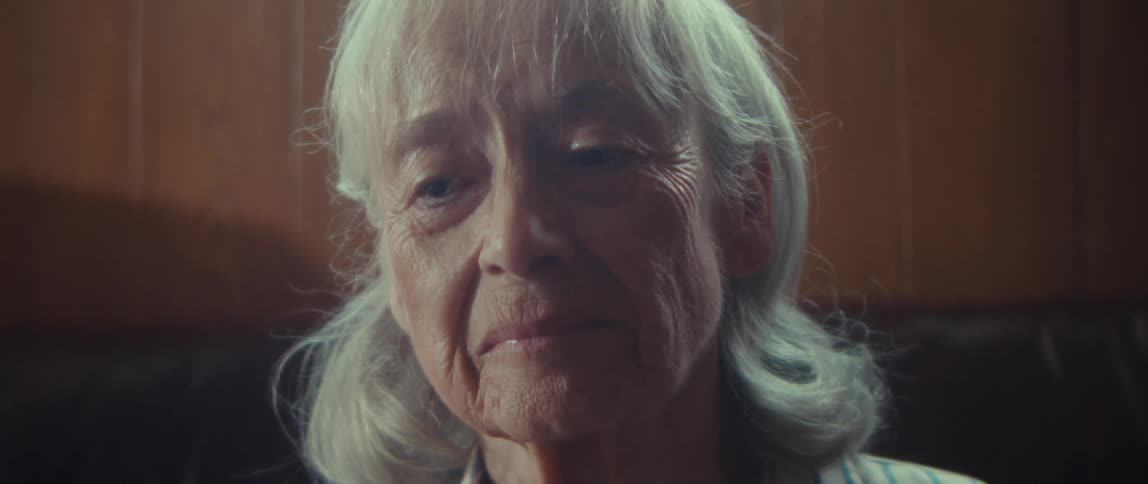 Elderly woman with a sad expression sitting on a sofa in a living room
