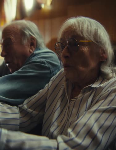 An older man and an older woman with gray hair show excited openmouthed expressions while actively playing a video game together indoors