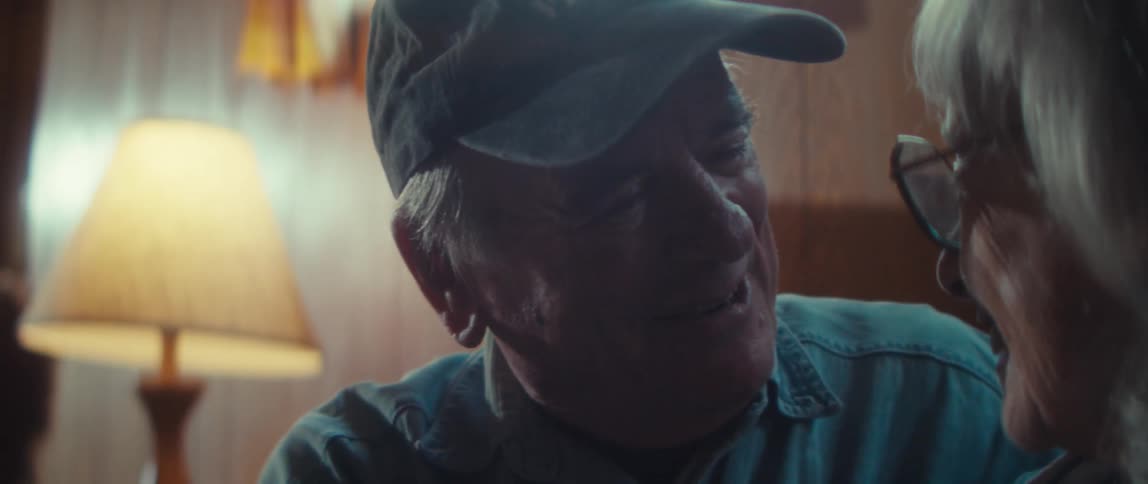 Close up of an elderly man and woman hugging each other while sitting in a living room during daytime