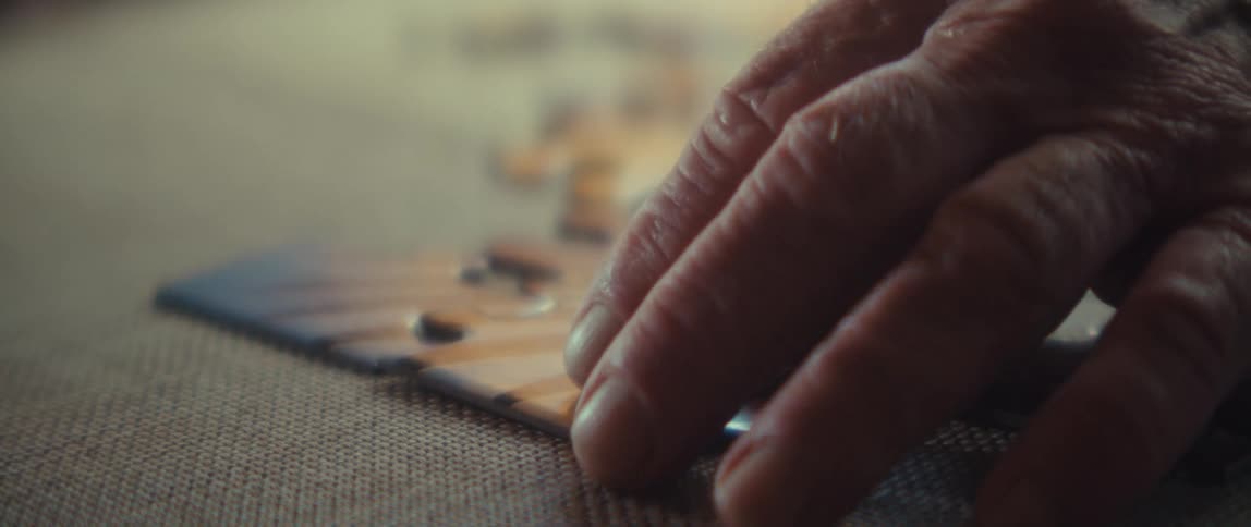 An elderly mans hand is solving a jigsaw puzzle on a bed