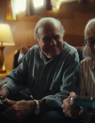 An elderly couple is playing a video game while laughing and joking