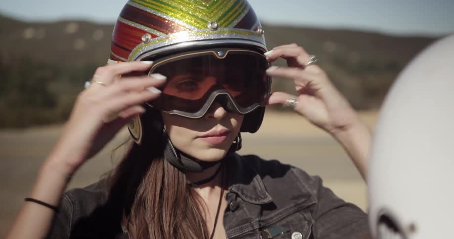 A woman wearing a motorcycle helmet puts her goggles on