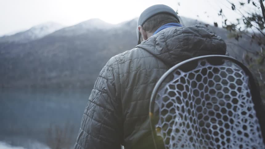 The man carries his fishing pole towards the mountain