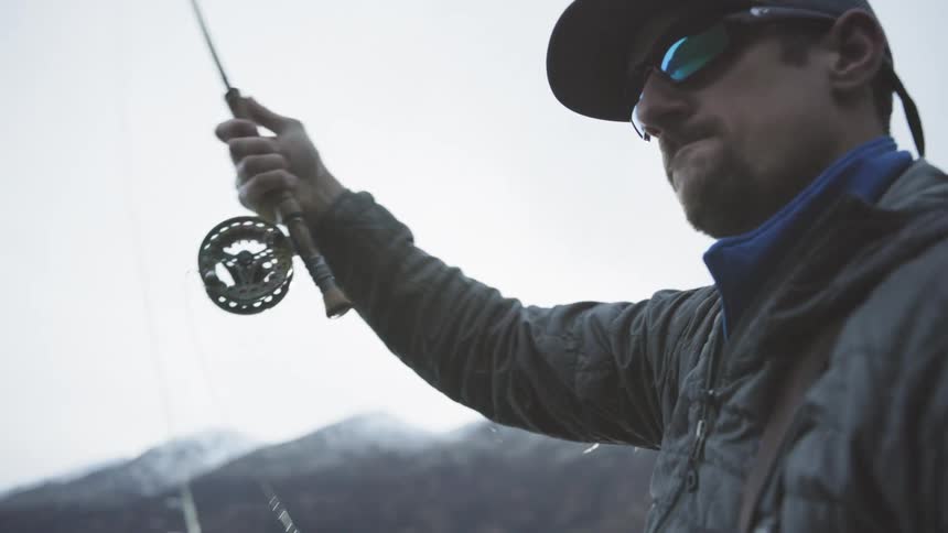 Man casts his fishing line while the sun peeks over the mountains