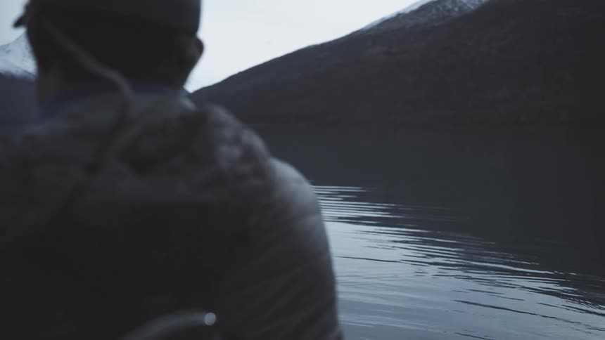 The man casts his fishing rod out in the lake by the mountains
