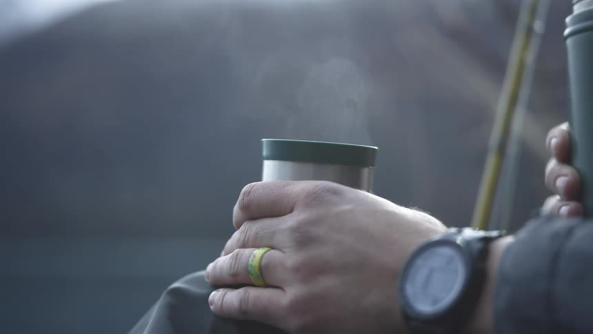 Close up of a young man holding a cup containing a hot drink while outdoors during daytime