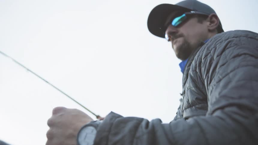 A man wearing sunglasses swings his fishing rod back and forth