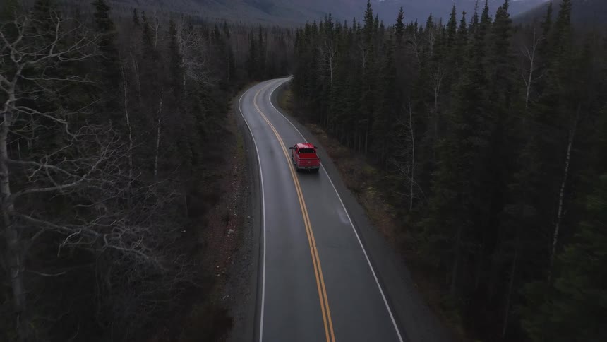 The red truck travels down the road surrounded by trees