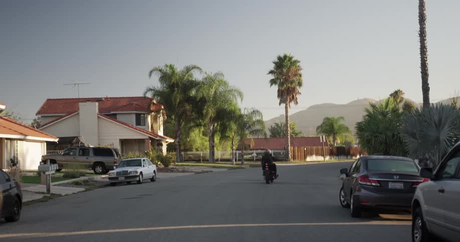 A man and woman ride a motorcycle down a suburban street