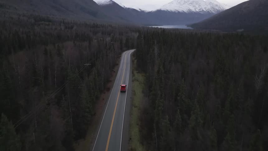 Red vehicle traveling on a road surrounded by forest with mountains in the background