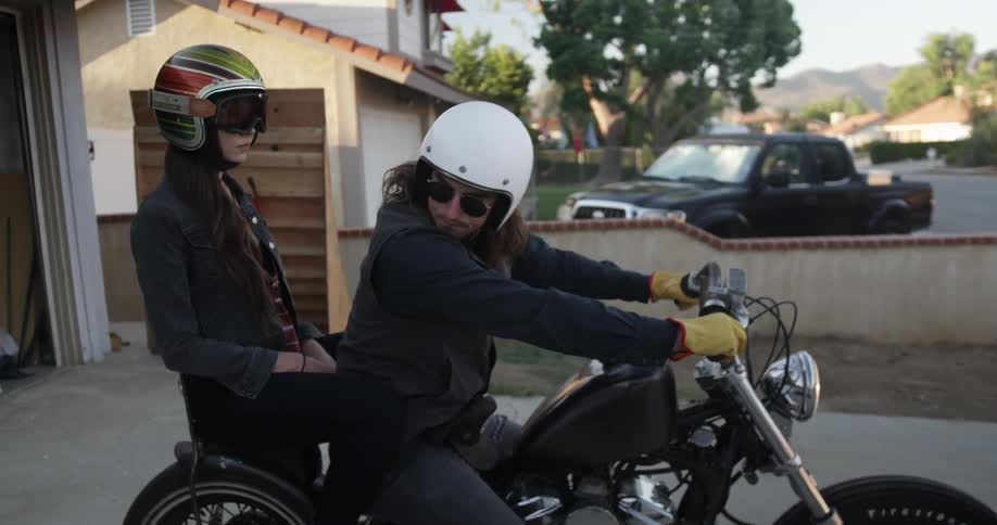 A man on a motorcycle with a female passenger looks to the side