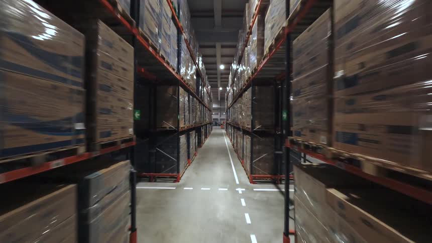 Plastic wrapped cardboard boxes fill the shelves lining an aisle in a warehouse