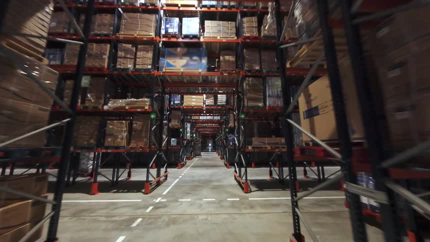 Warehouse aisle with tall metal racks filled with stacked boxes