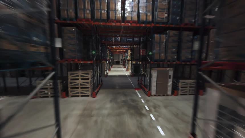 Interior warehouse aisle with tall metal racks filled with stacked pallets