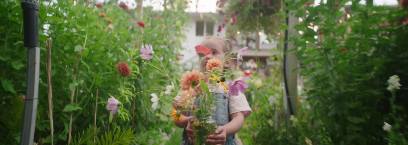 Child walks through a blooming garden holding a jar of colorful flowers