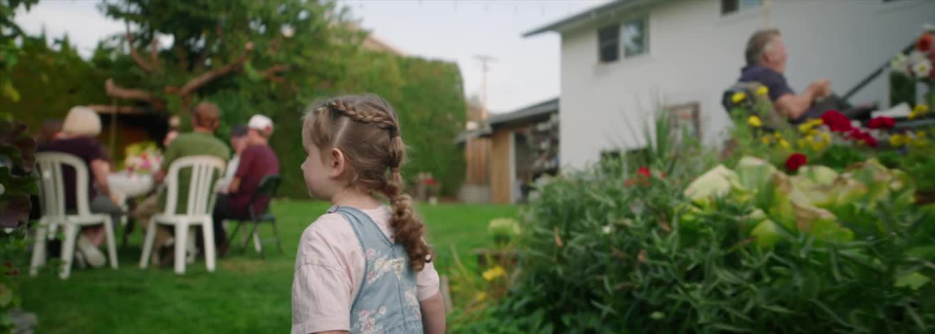 A young girl walks along a garden path surrounded by foliage