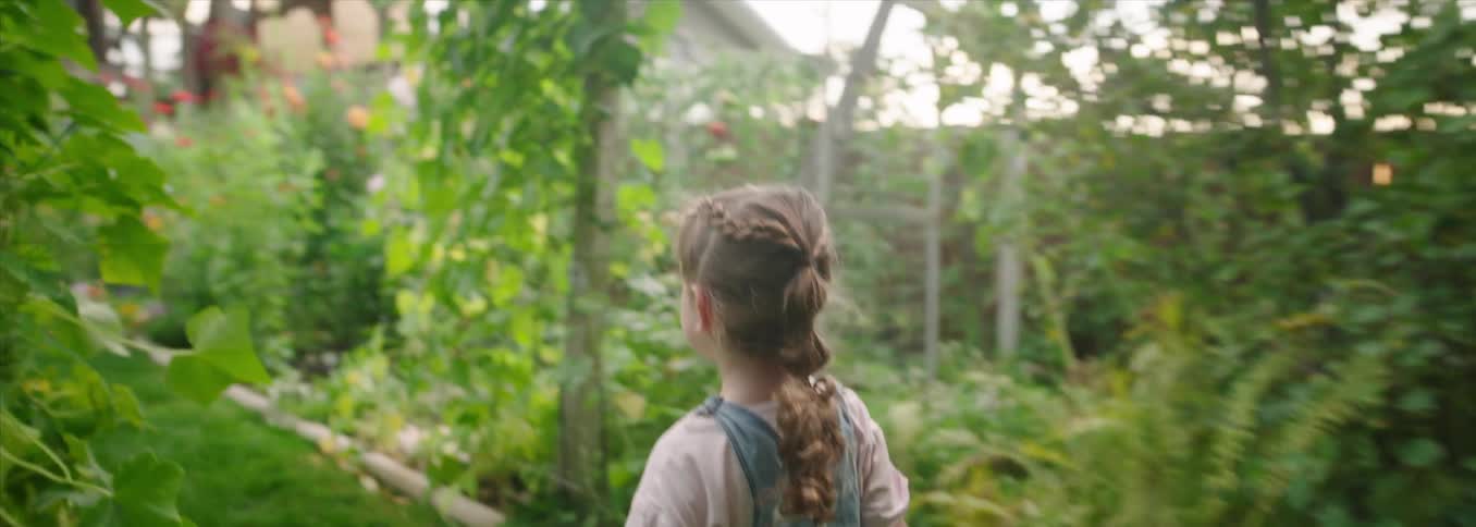 Child walking through a garden surrounded by foliage and flowers