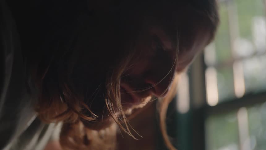 Longhaired man leaning under soft light near a window