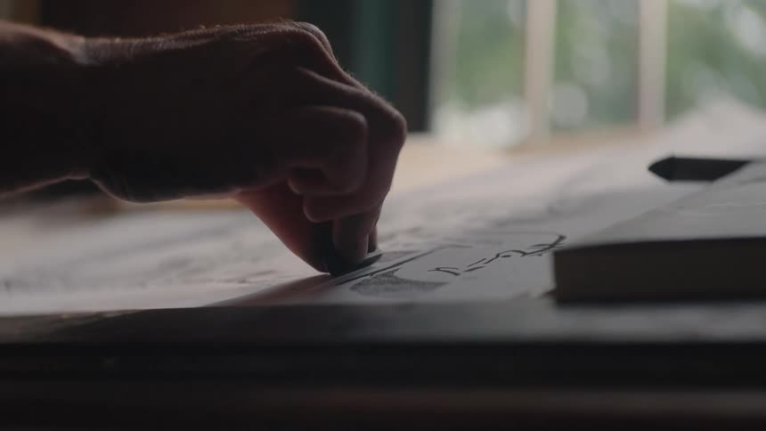 Closeup of a hand sketching on paper at an indoor table