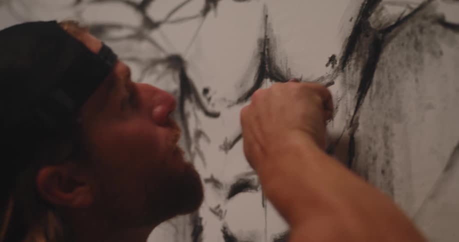 Person wearing a cap drawing or painting black art on a white wall