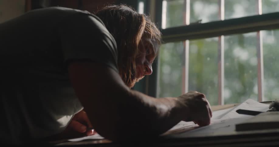 Man writes with focus at a table lit by natural light coming through the window