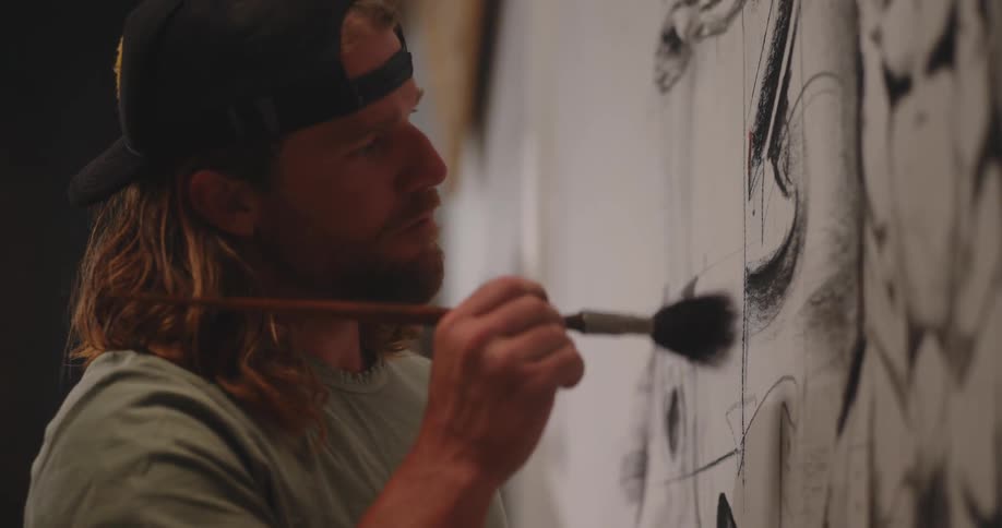 Man paints details on a large canvas using a brush with delicate strokes