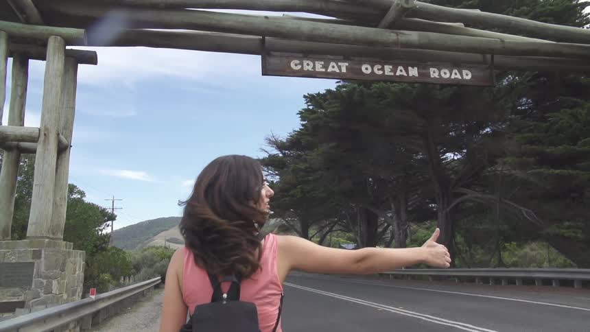 A woman hitchhikes by a road